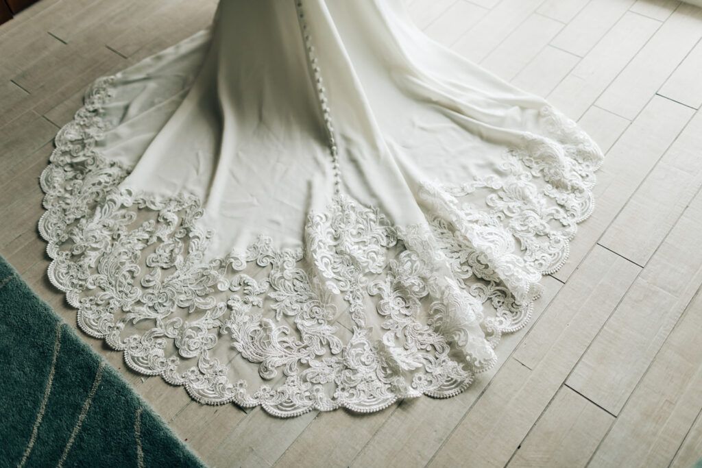 White wedding dress train with lace trim on wood floor next to a blue rug.