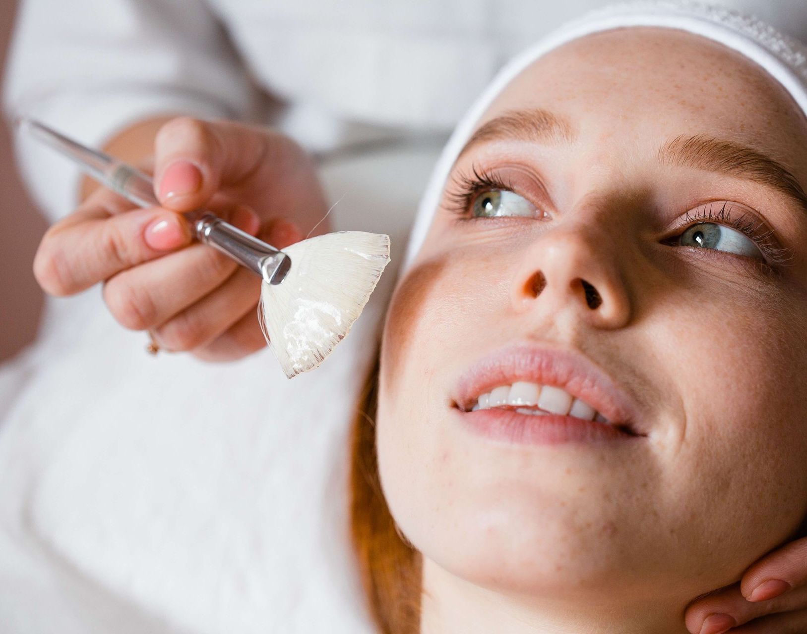a woman is getting a facial treatment with a pink brush