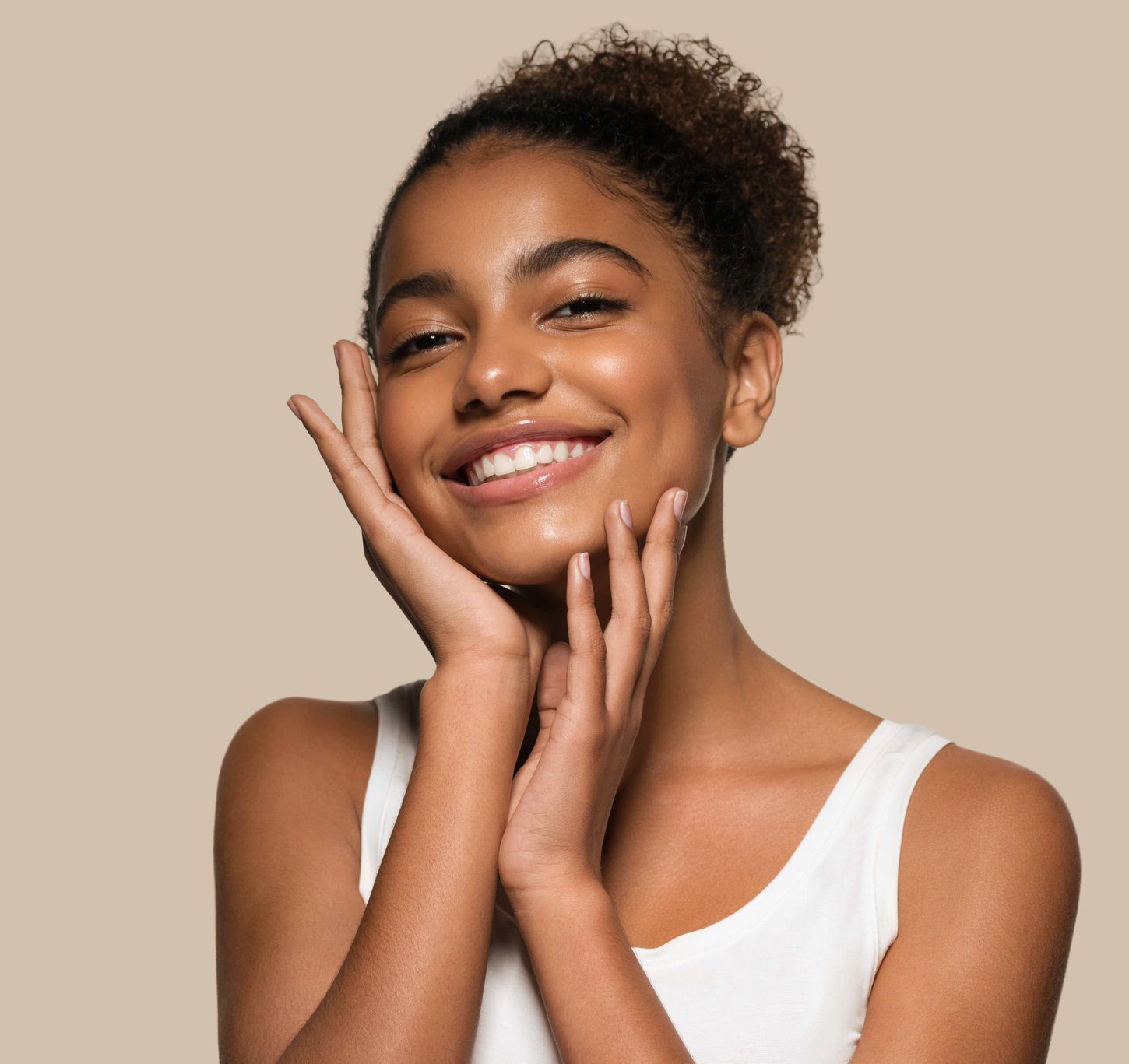 a woman in a white tank top smiles with her hands on her face