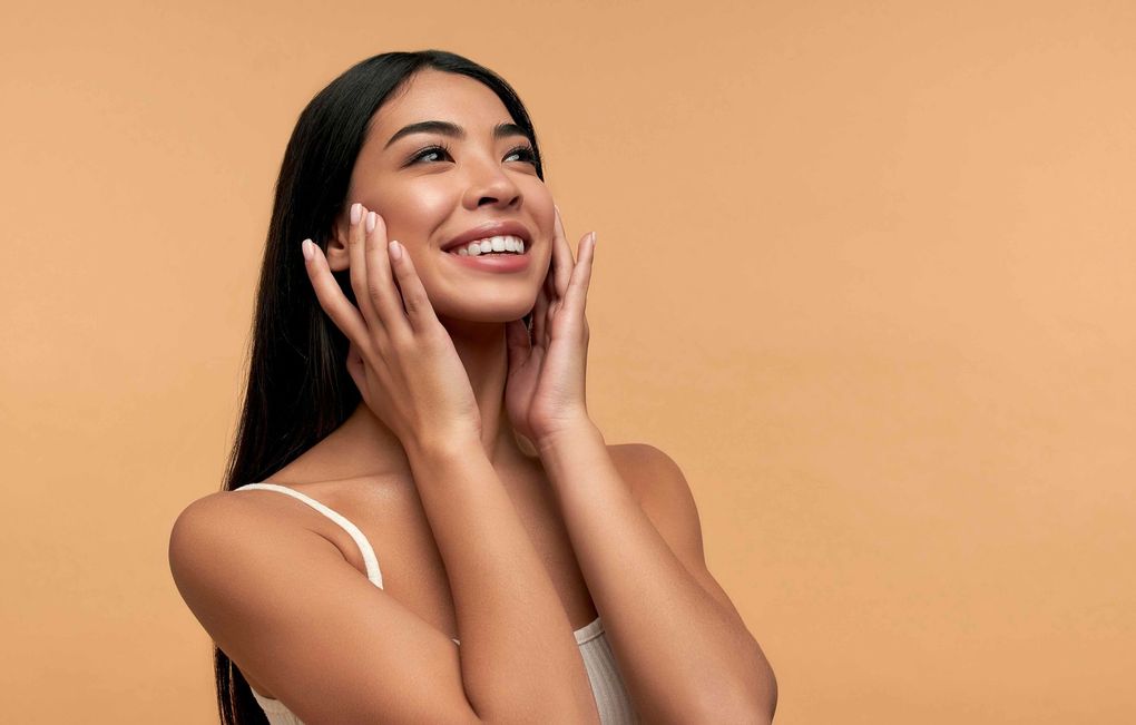 a woman is smiling and touching her face with her hands.