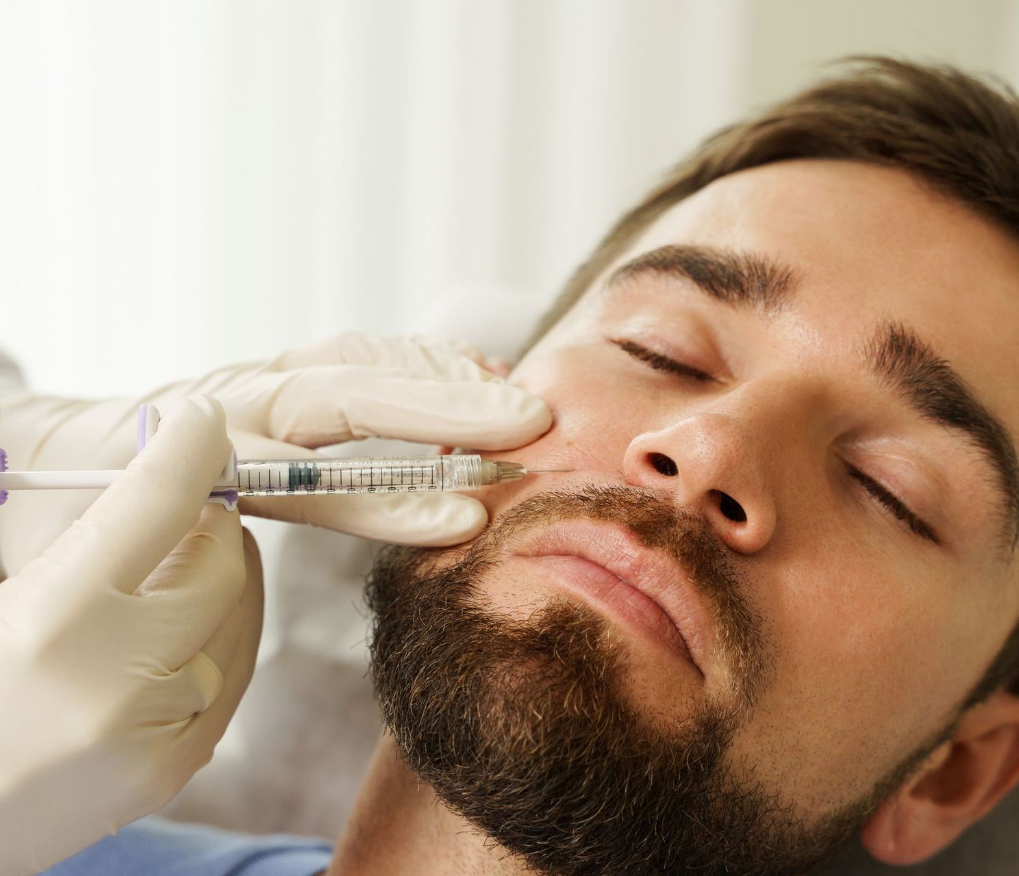 A man with a beard is getting a botox injection in his face.