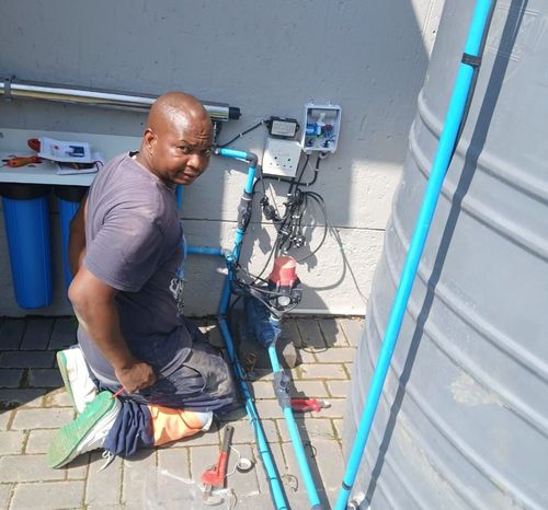 A man is kneeling down next to a blue pipe