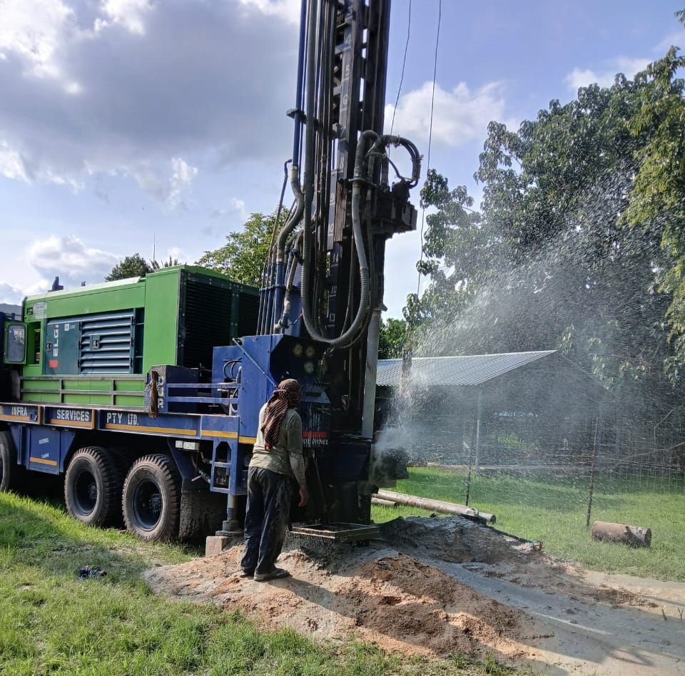 A man is standing next to a large machine that is drilling a hole in the ground.
