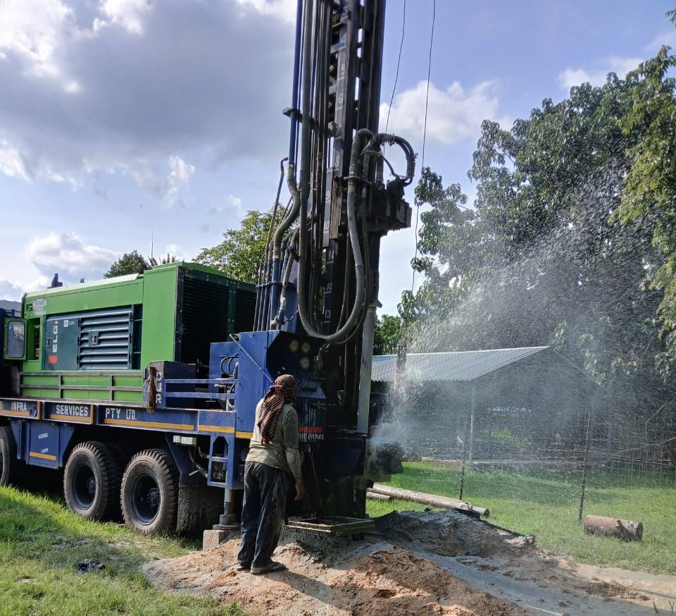 A man is standing in front of a large green and blue borehole drilling machine