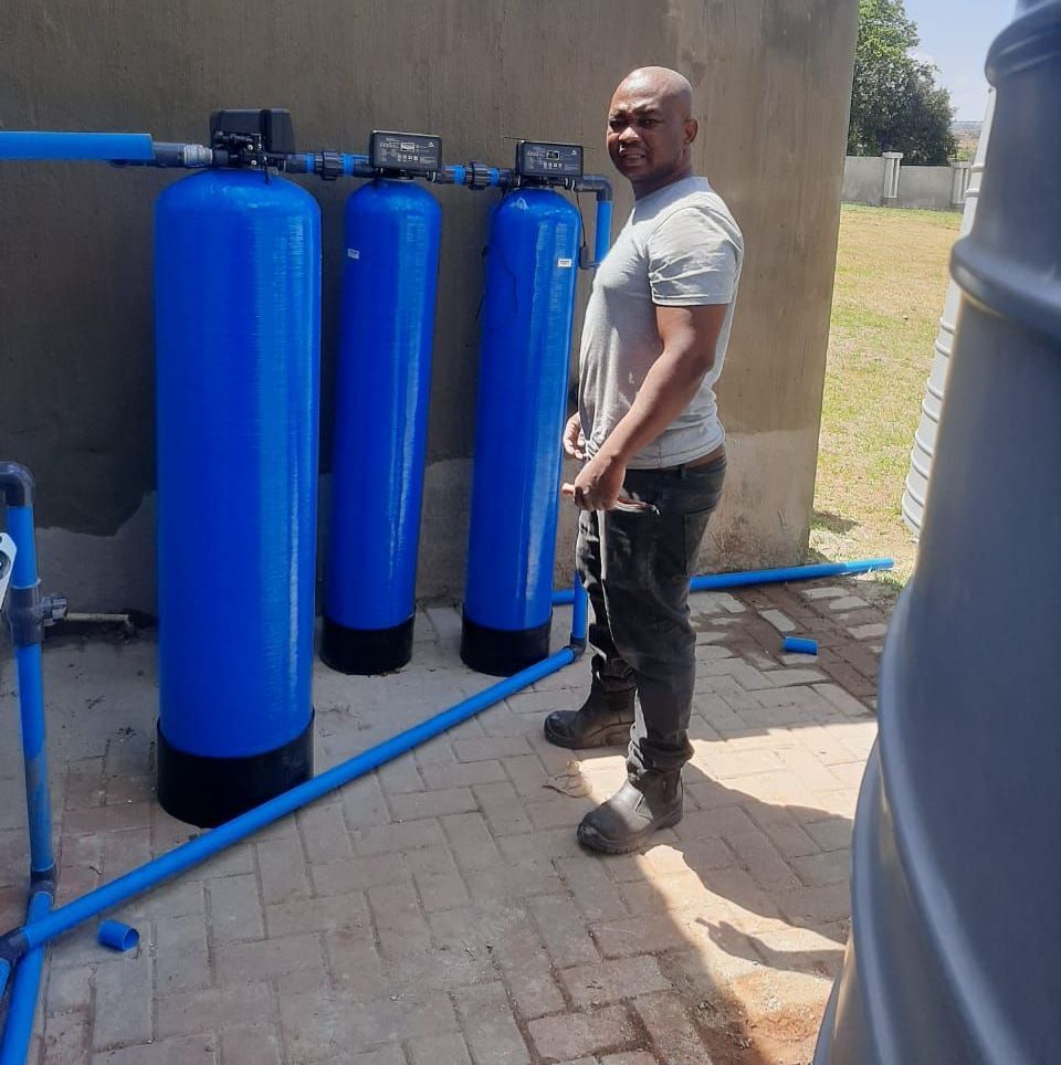 A man is standing in front of a row of blue water filter tanks