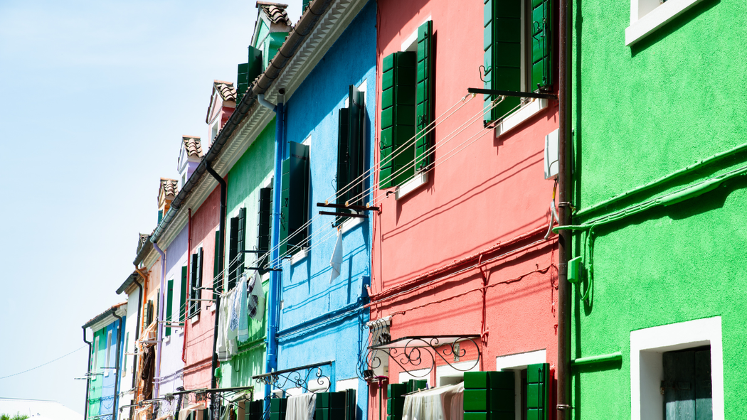 Row of brightly colored houses in blue, pink, green, and orange with shutters and laundry lines.