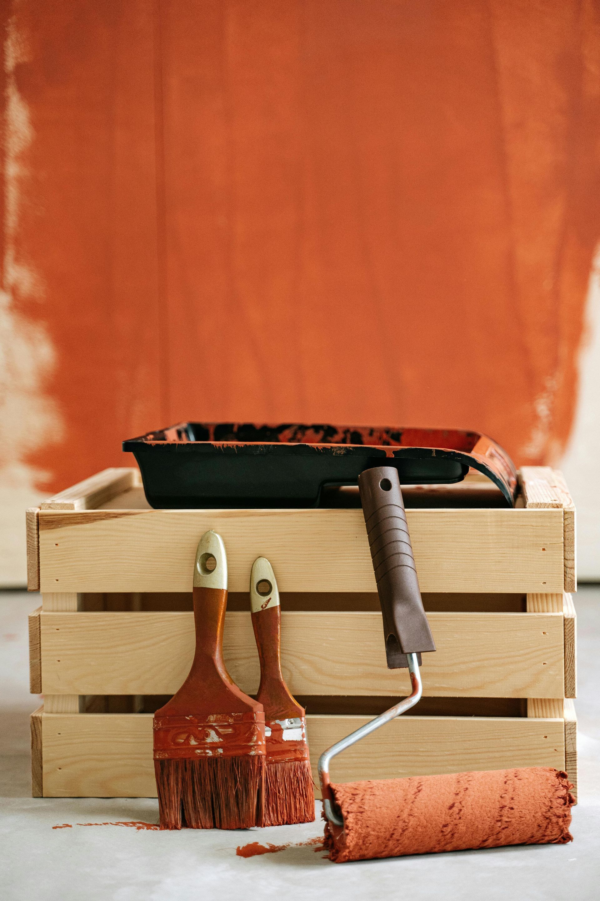 Paint supplies on wooden crate in front of a wall with reddish-orange paint.