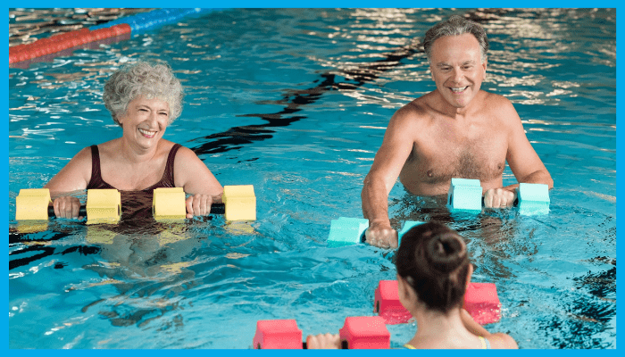 Older adults in an aqua aerobics class using foam dumbbells under instructor guidance to aid recovery and mobility.