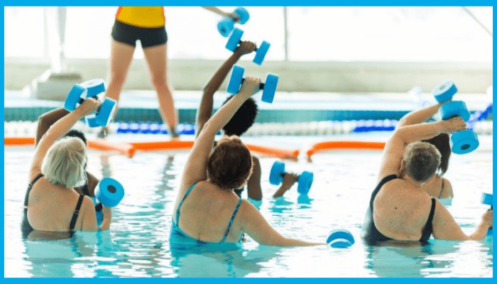 Group of adults in a swimming pool doing aqua aerobics with foam dumbbells for weight loss and fitness