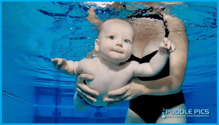 A calm baby being gently held underwater during a supervised swim lesson, demonstrating correct submersion technique.