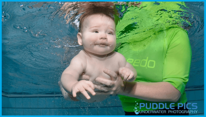 Baby gently supported underwater during swim lesson, showing subtle facial cues and body language to assess readiness.