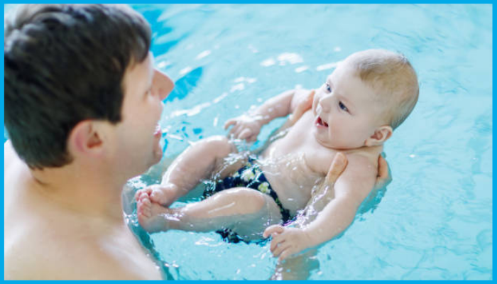 Baby smiling and looking at caregiver during a swim lesson, showing readiness for submersion with horizontal support.