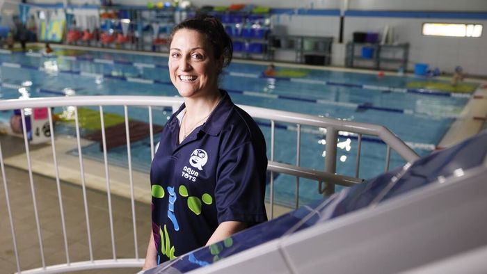 Alena Sarri smiles near an indoor swimming pool, leaning on a railing.