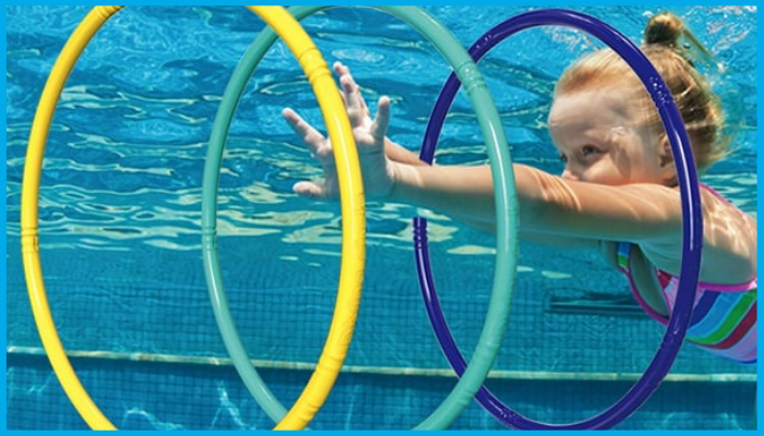 Child swimming underwater through colourful floating hoops in a pool, holding breath with face submerged.