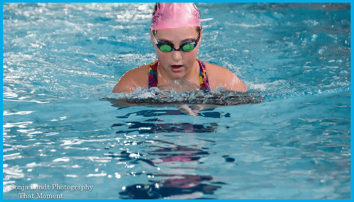 Young competitive swimmer in pink swim cap performing breaststroke during training