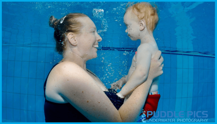 Parent holding baby underwater during an early swim lesson at a Canberra pool, both smiling and engaged in gentle water play.