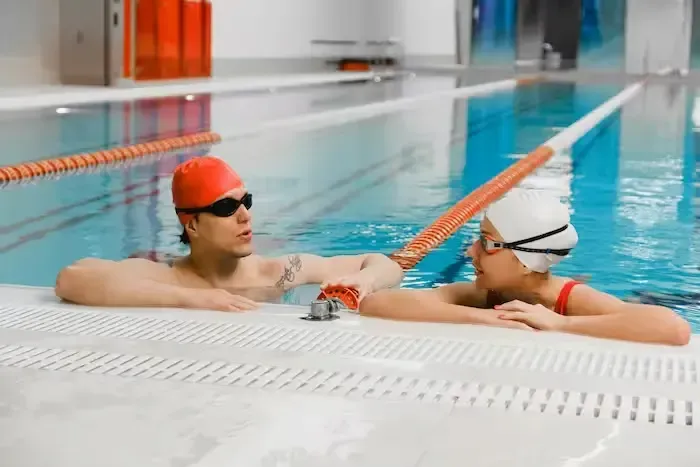 An adult male swim instructor supporting a young child in the water, teaching essential swimming skills for overall safety.