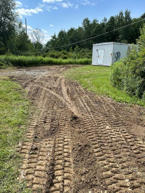 A dirt road leading to a white building in the middle of a field.