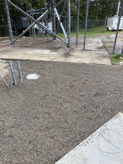 A concrete surface with gravel and a metal structure in the background.