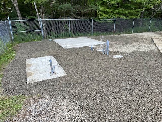 A gravel area with a fence and a concrete slab in the middle of it.