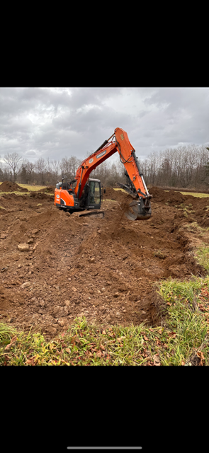 A large orange excavator is moving dirt in a field.