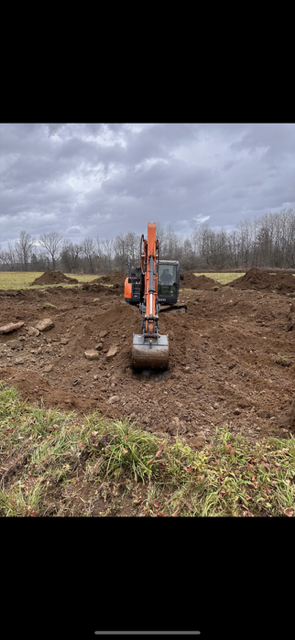 A large excavator is sitting in the middle of a dirt field.