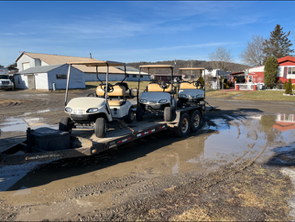Two golf carts are on a trailer in a muddy area.