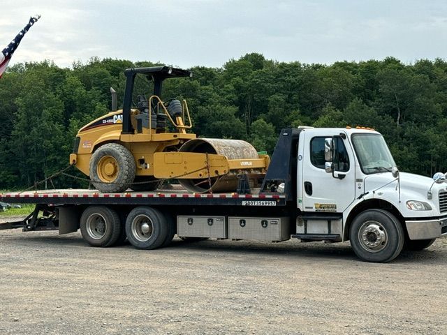 A tow truck is carrying a yellow roller on the back of it.
