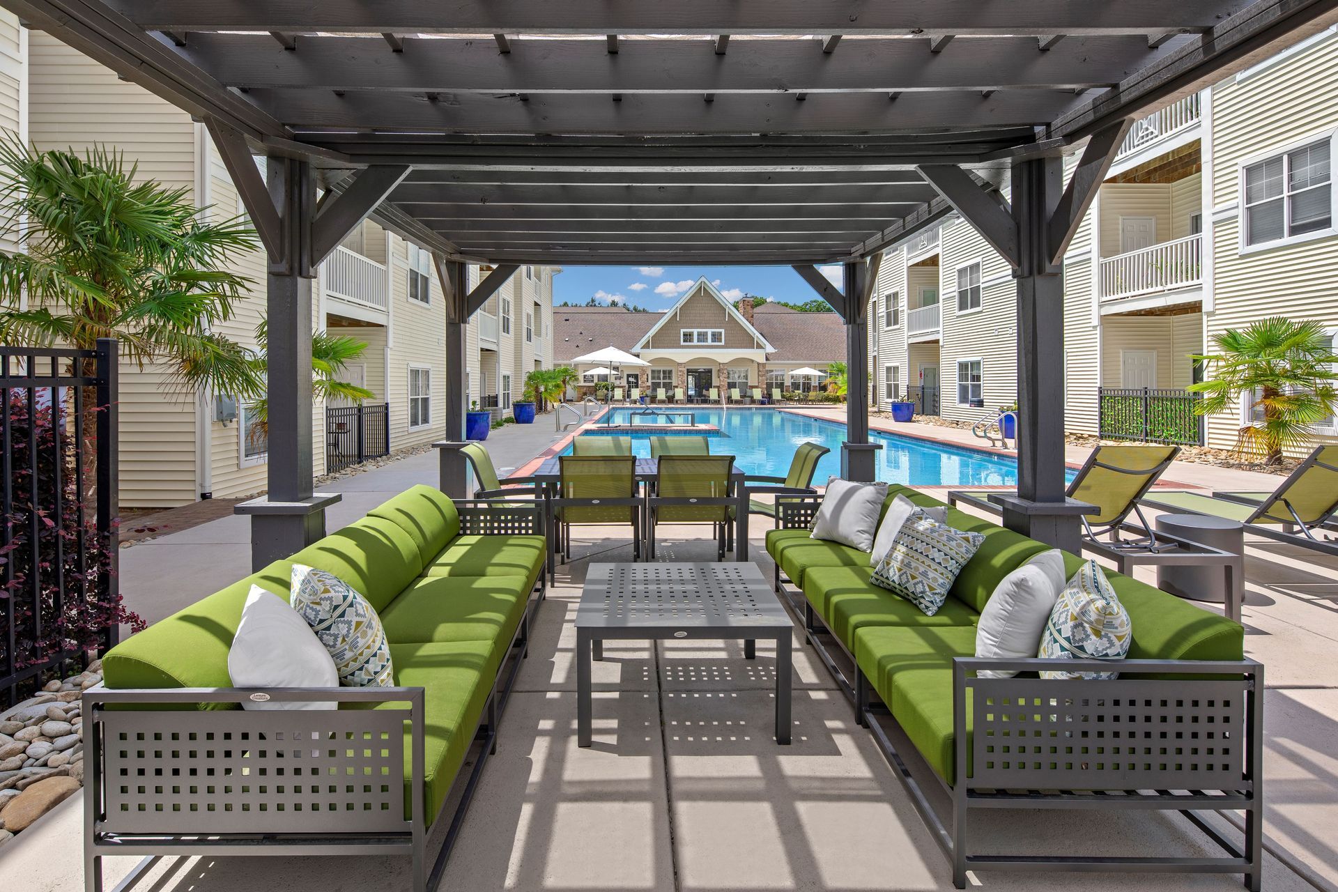 a pergola overlooking a swimming pool with green couches and chairs