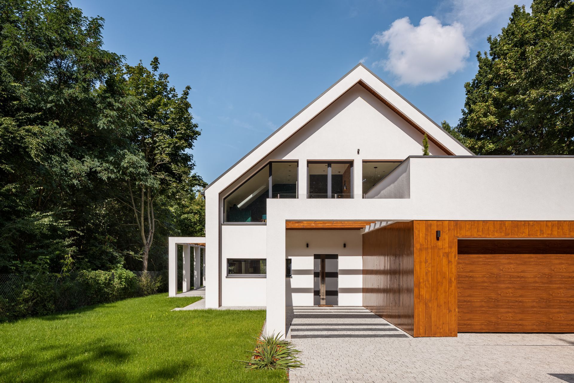 A white house with a wooden garage door is surrounded by trees.