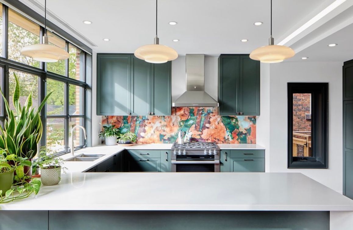 A kitchen with green cabinets , a stove , a sink , and a large island.