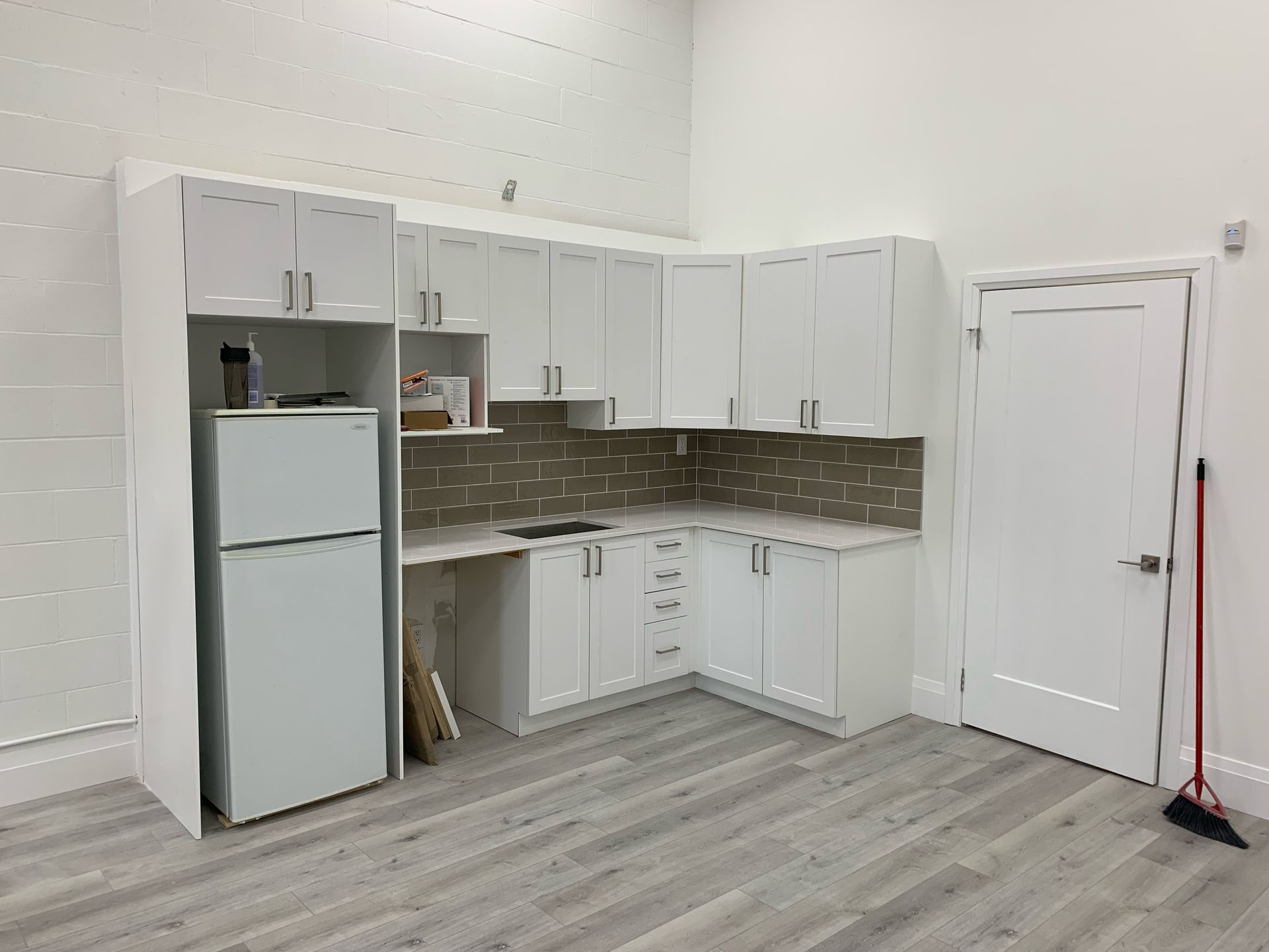 White kitchen cabinets and refrigerator in a bright room with a door.