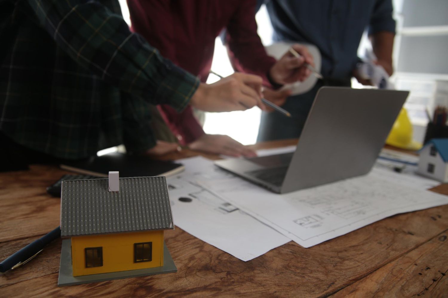 A group of people are sitting at a table with a laptop and a model house.