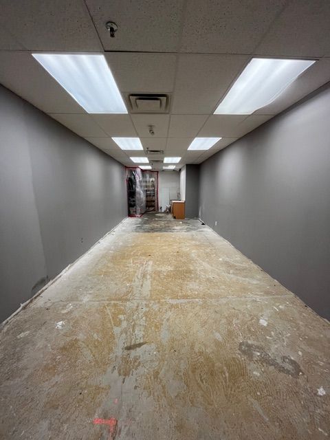 Empty commercial space with gray walls, overhead lights, and bare concrete floor.