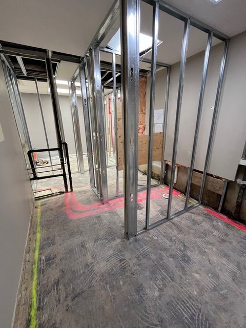 Interior under construction: metal studs frame walls; unfinished flooring; spray paint marks.