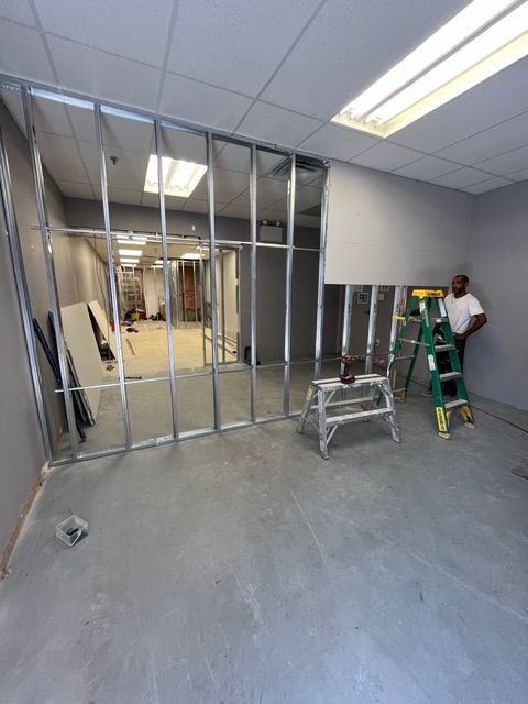 Metal framing for an interior wall under construction. A person stands near a ladder. Gray room.
