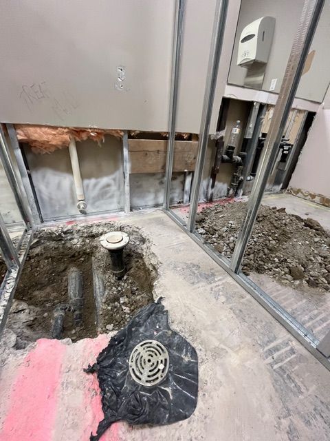 Bathroom under construction: exposed pipes, floor drain, framing, and debris.