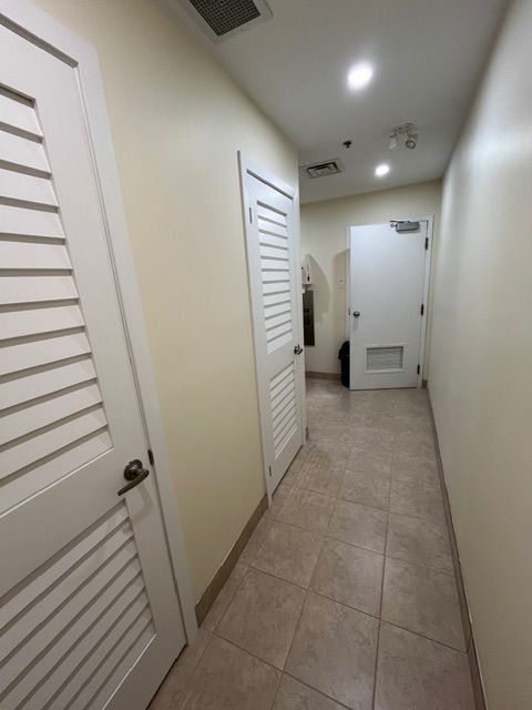 Narrow hallway with tiled floor, white doors, and cream-colored walls.