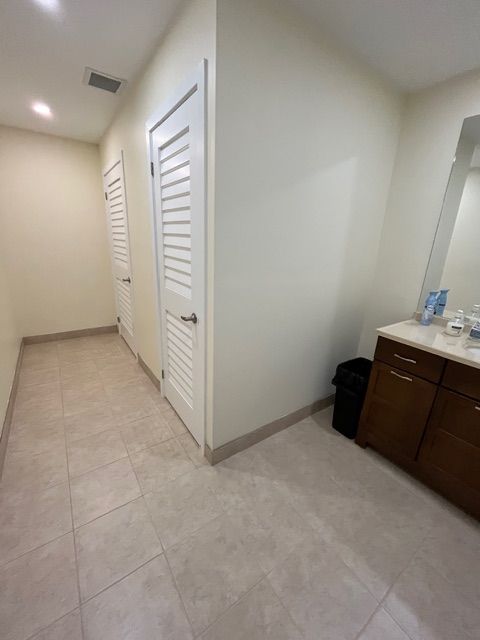 Narrow hallway with two white doors, tile floor, and a dark wooden vanity.