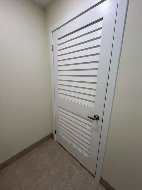 White louvered door in a beige room with a dark handle, leaning open.