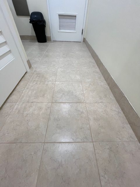 Tan tiled floor in a hallway with a white door, a pet door, a black trash can, and beige trim.