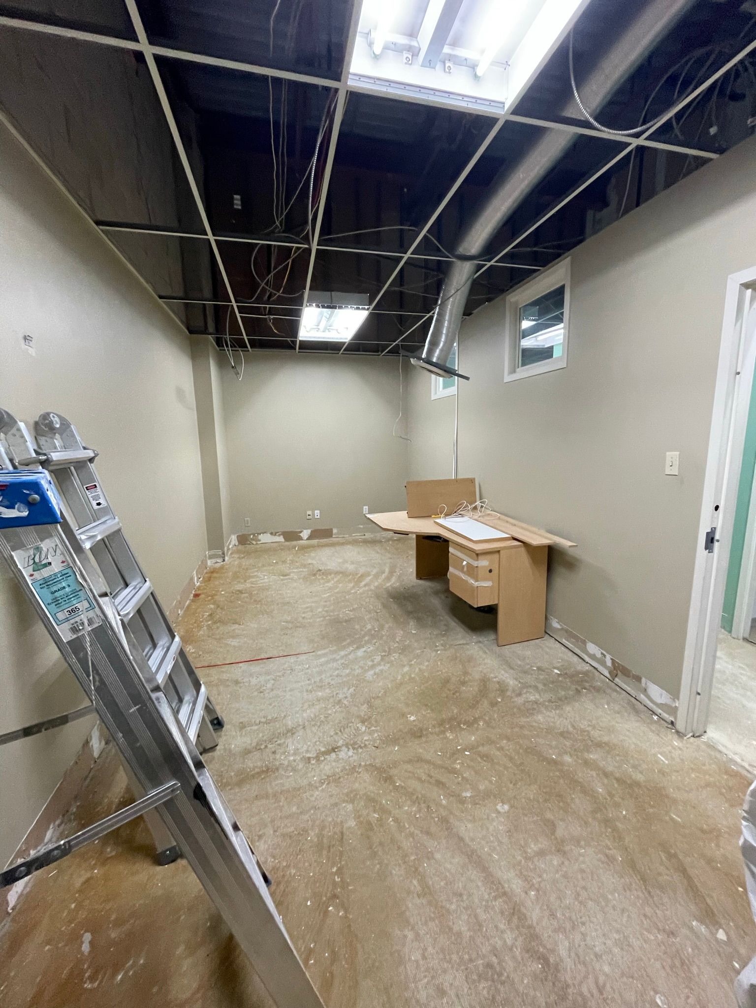 Interior room under construction, ladder, desk, exposed ceiling, walls, light, debris on floor.