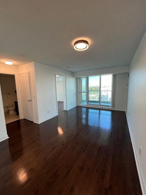 Empty room with dark wood floor, white walls, and a large window.