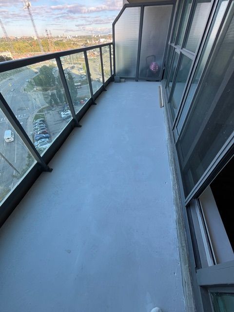 Balcony with light gray floor, glass railings, and a partially obscured person.