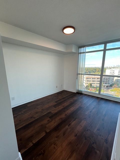 Empty room with dark hardwood floors, white walls, and large windows.
