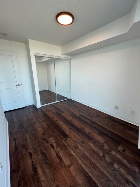 Empty room with dark wood floor, white walls, mirrored closet doors, and a round ceiling light.