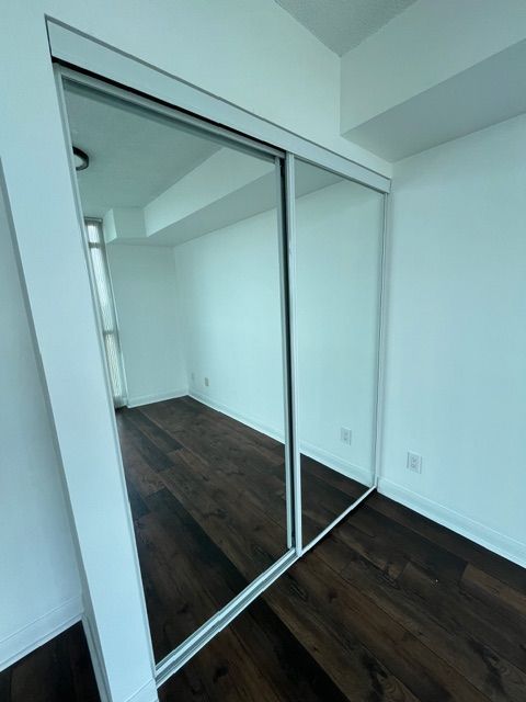 Empty room with mirrored sliding closet doors and dark hardwood floors.