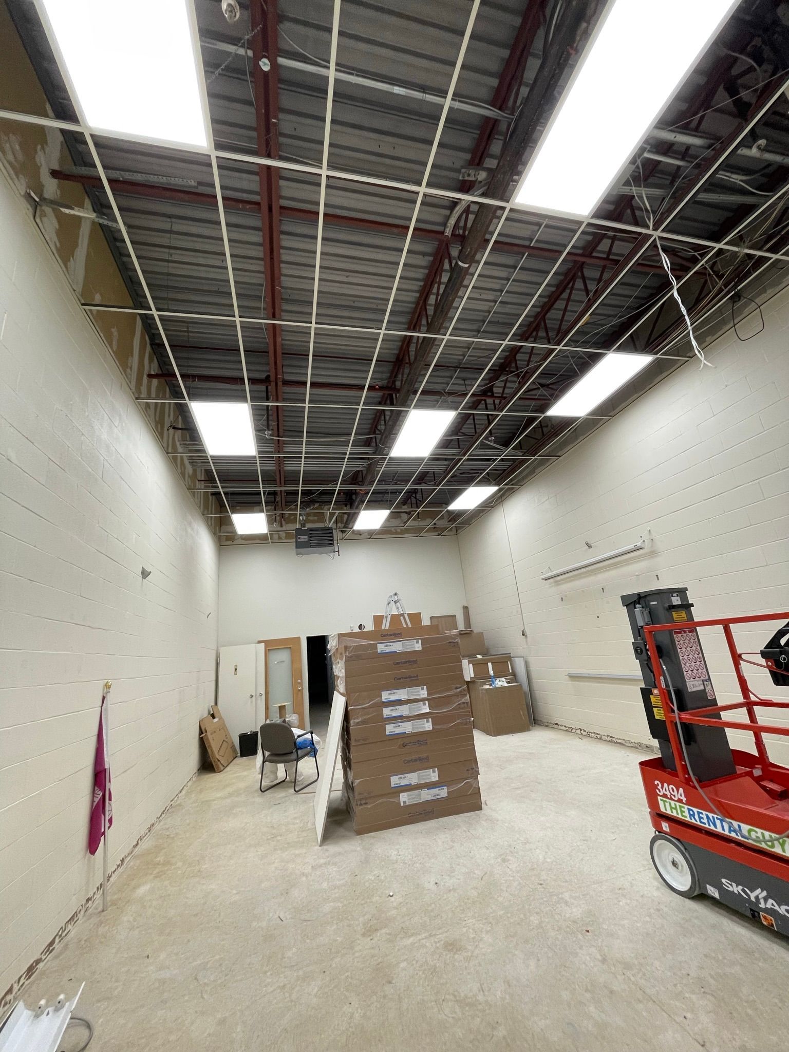 Interior of a commercial space under construction with exposed ceiling, boxes, and a lift.