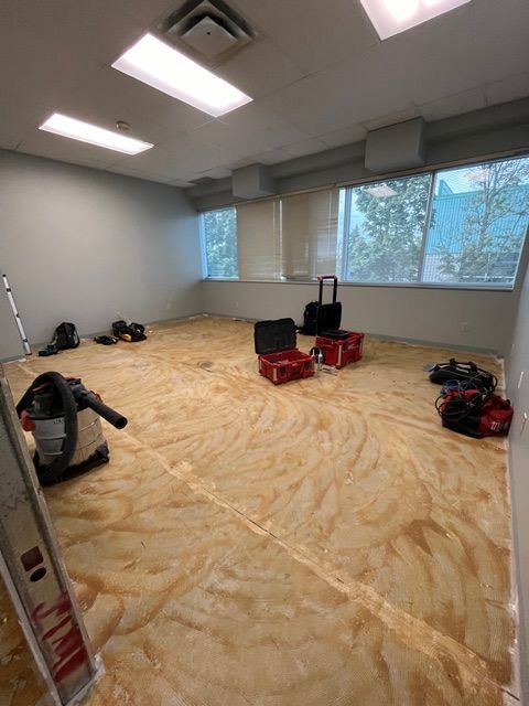 Room under construction; plywood floor, tools scattered, windows, overhead lights.