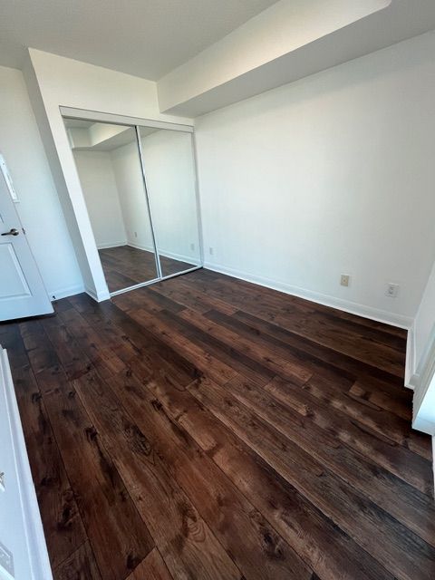 Empty room with dark wood floor, white walls, and a mirrored closet door.